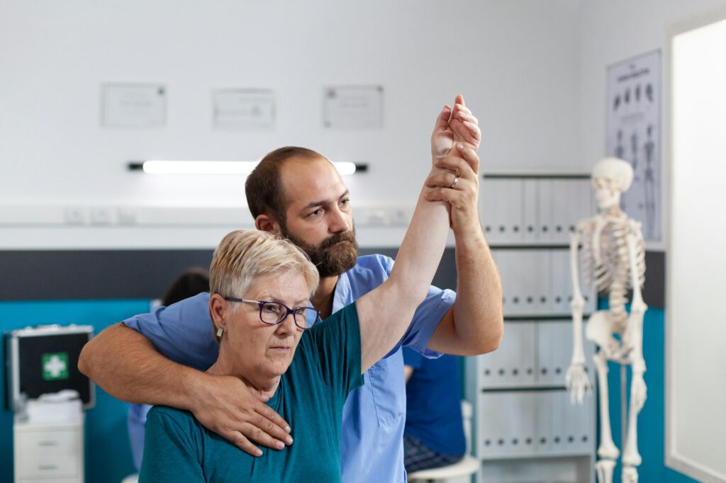 Chiropractor stretching arm muscles of elder woman with injury