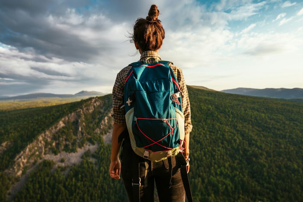 A tourist girl with a backpack admires the sunset from the top of the mountain.