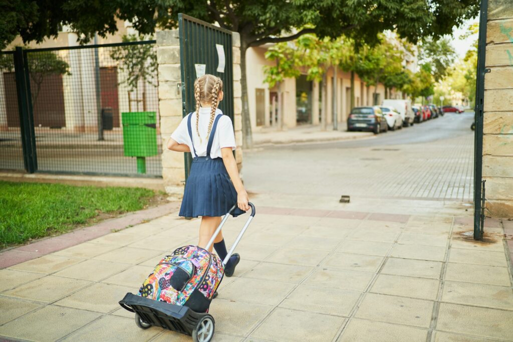 Unrecognizable spanish school girl riding her wheeled backpack to go out